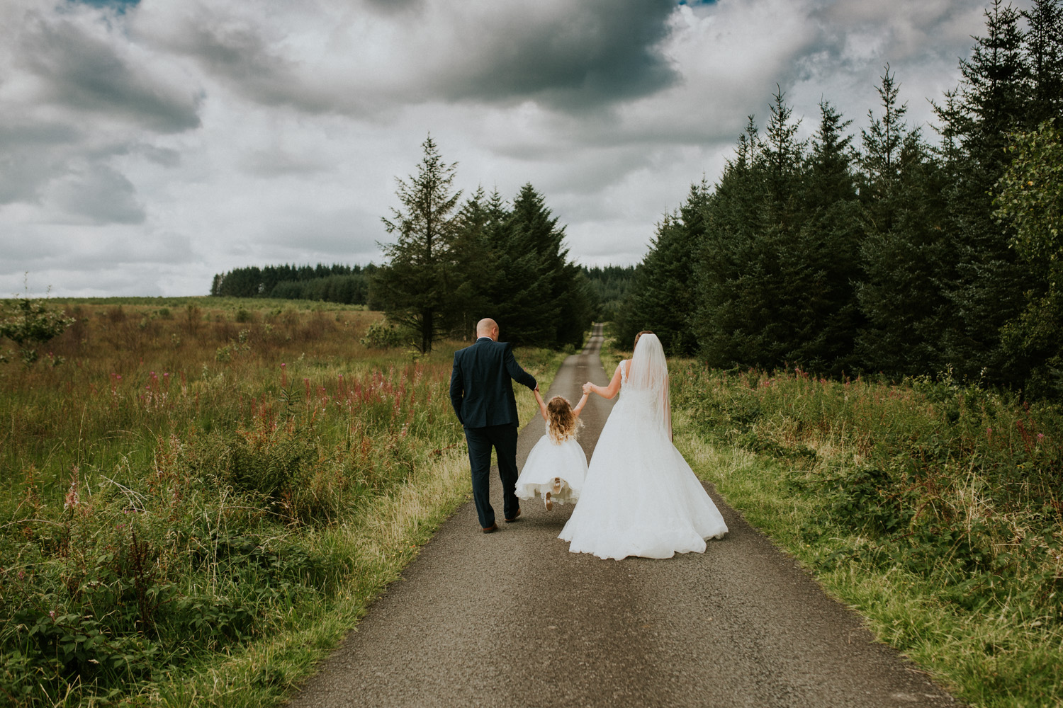 bride groom and daughter walking down woodlands